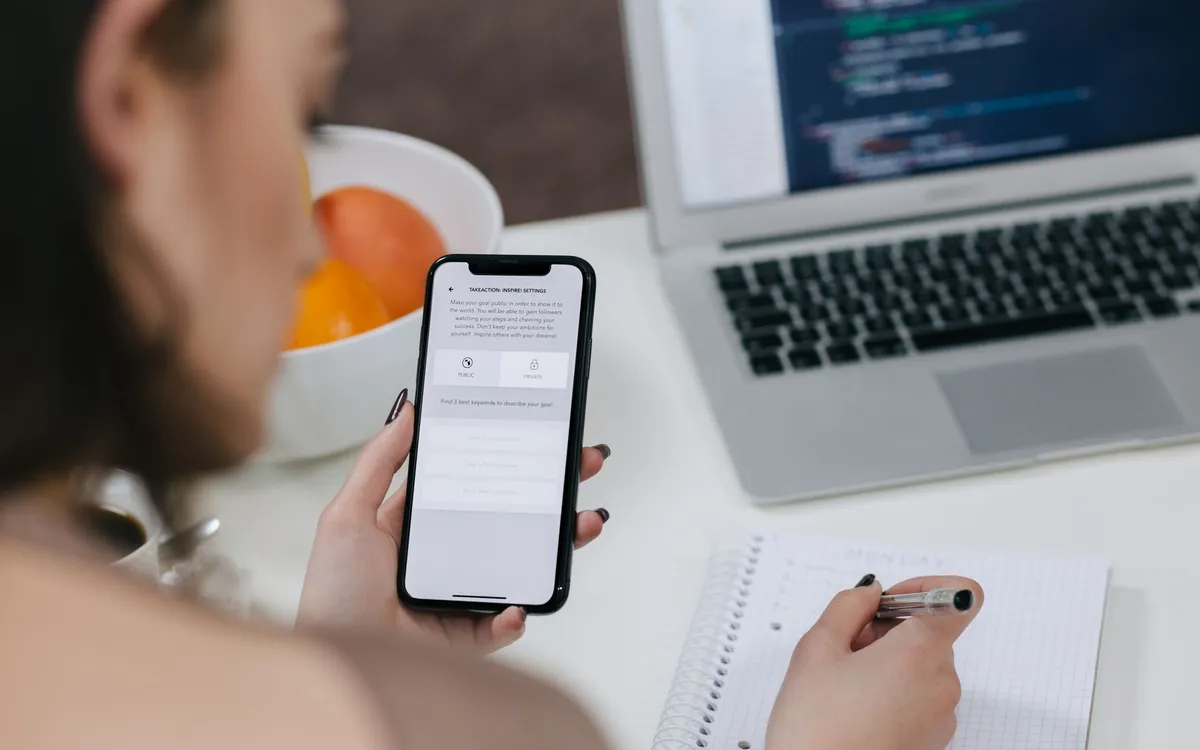 Pessoa usando o celular diante de um notebook com código na tela